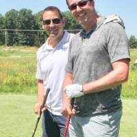 two alumni pose with their golf clubs
